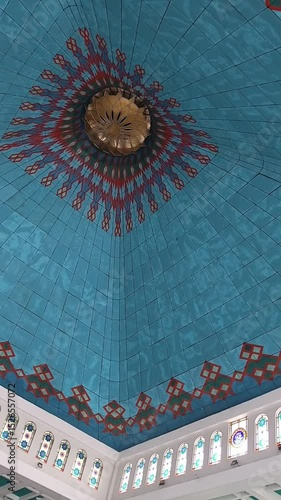Stunning upward view of a mosque dome featuring intricate geometric Islamic art in turquoise and gold. The symmetrical design and vibrant colors reflect traditional Muslim architecture and spiritualit
