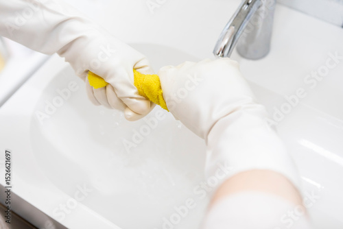 Close-up shot of woman in rubber gloves cleans sink and faucet with a rag and spray in the bathroom. Household and cleaning concept