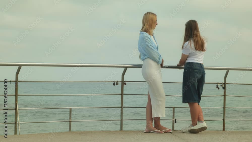 Mother and teenage daughter sharing quiet moment by metal railing, embracing and gazing across ocean horizon, connecting through peaceful family experience near seaside Mother and teenage daughter sharing quiet moment by metal railing, embracing and gazing across ocean horizon, connecting through peaceful family experience near seaside