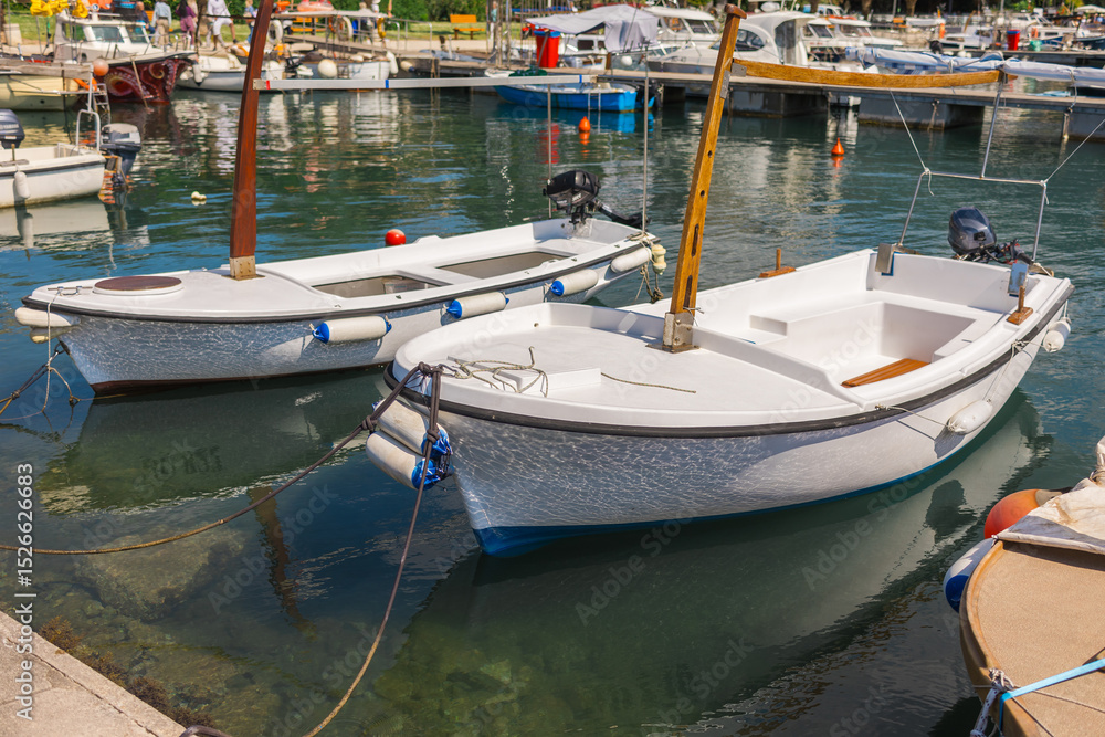 Obraz premium Small fishing boats anchored in clear harbor water. Coastal lifestyle, traditional transport, and peaceful summer atmosphere at the marina.