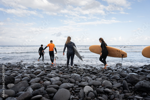 Surfers walking on rocky beach with surfboards entering ocean for surfing session