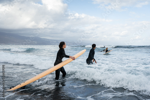 Photography Surfers walking into ocean with surfboards, preparing to surf waves