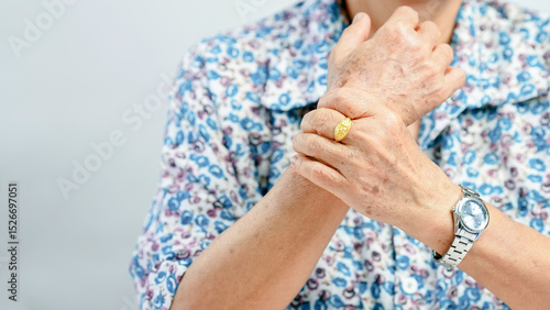 Schilderij op canvas Elderly person wearing floral shirt, holding their wrist with one hand, gold rin