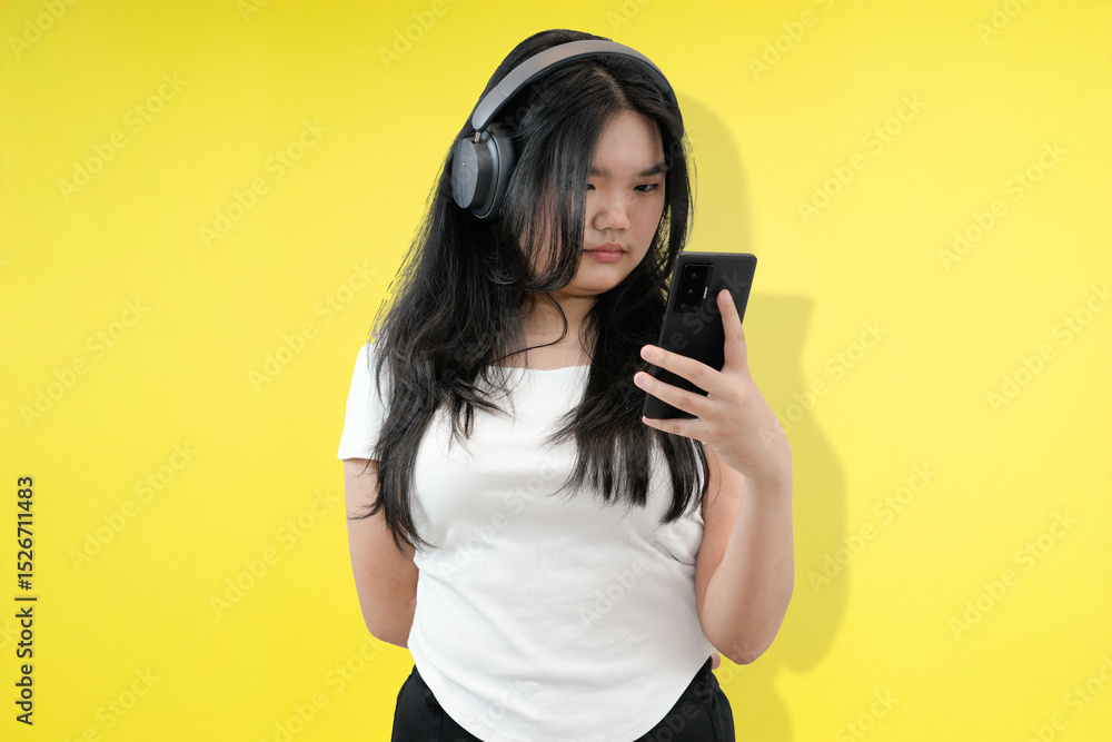 Obraz premium young asian woman seriously looking at phone with headphone in yellow studio background