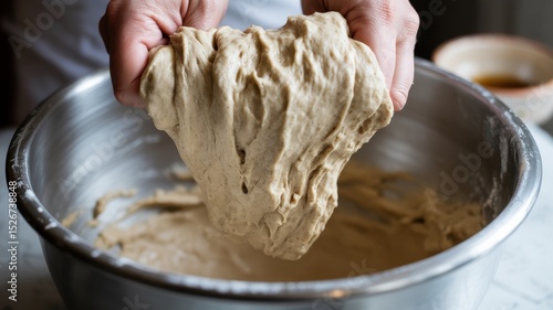 Female hands stretching fermented sourdough in metal bowl for homemade bread making