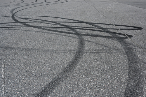 an asphalt surface covered in overlapping tire skid marks from high-speed driving maneuvers such as drifting or burnouts