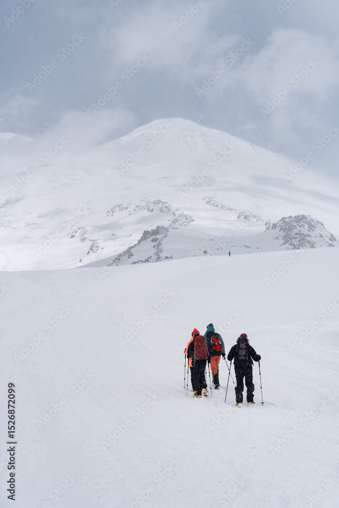 Group of climbers with backpacks and trekking poles making their way up the snowy slopes of Mount Elbrus under a dramatic cloudy sky Group of climbers with backpacks and trekking poles making their way up the snowy slopes of Mount Elbrus under a dramatic cloudy sky