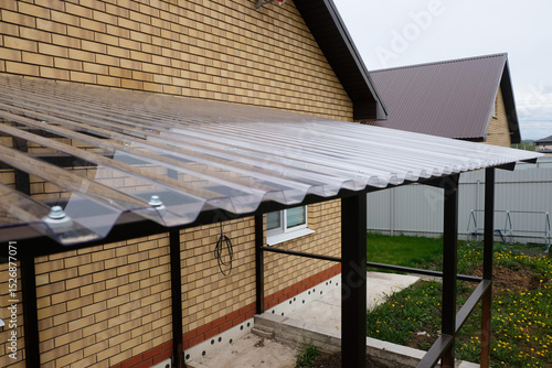 Canopy of a country house terrace made of metal structures and transparent roof made of profiled polycarbonate, construction process