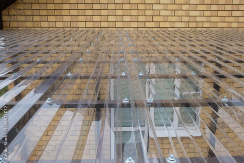 Fragment of transparent roof made of profiled polycarbonate with fastening elements in form of thermal washers and self-tapping screws, canopy made of metal structure for  terrace of country house