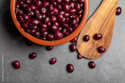 Earthenware bowl full of Anguiano red beans with a wooden spoon on a kitchen worktop in a zenithal photograph.