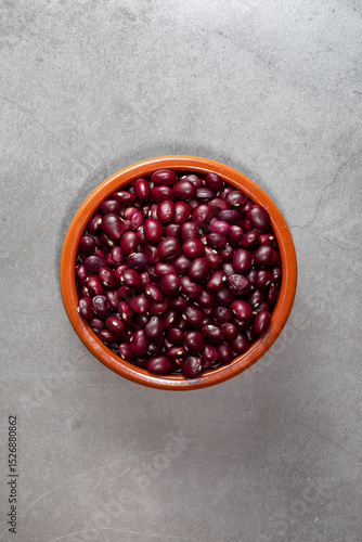 Earthenware bowl full of Anguiano red beans with a wooden spoon on a kitchen worktop in a zenithal photograph.