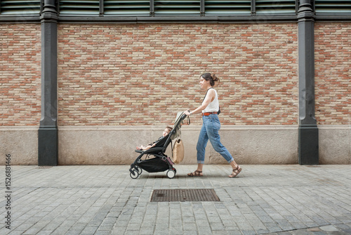 Side view of mother walking with stroller past decorative brick wall