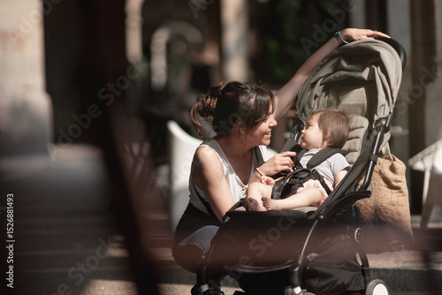 Mother kneels beside stroller to talk to her baby during city walk