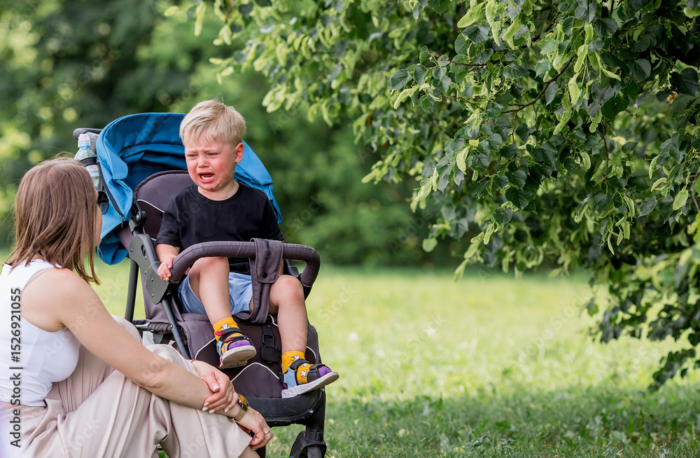A little boy in a stroller and his mom. Childish hysteria. The child screams, cries, gets cranky and gets hysterical. Discontent. A little boy in a stroller and his mom. Childish hysteria. The child screams, cries, gets cranky and gets hysterical. Discontent.