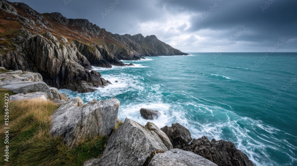 Fototapeta premium Strong waves crash against rocky cliffs on a dramatic coastline as dark clouds gather overhead, creating a moody atmosphere during early evening hours.