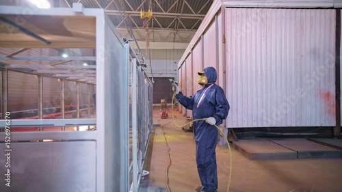 Worker sprays metal structure in industrial workshop during daytime production process