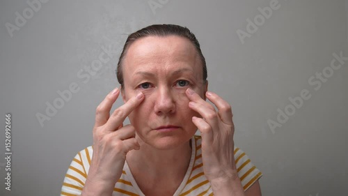 50-55-year-old woman looks with chagrin at her face with wrinkles, puffiness, and flabby skin. Age-related changes and fatigue. A woman is planning anti-aging procedures or plastic surgery