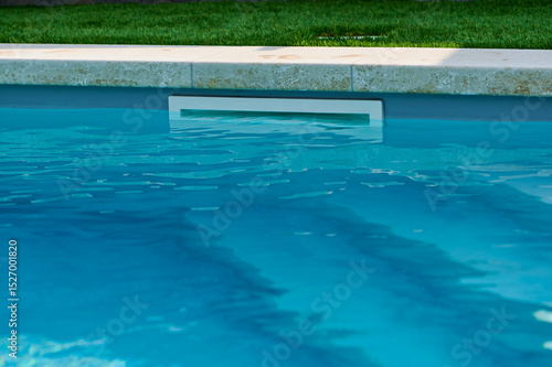 Swimming pool with clear blue water and pool cleaner in well-maintained backyard setting during sunny day