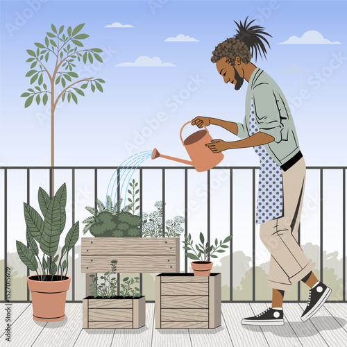 A young man is watering plants on a balcony using a watering can. There are wooden planters with various herbs and flowers around him. A large potted plant stands nearby. In the background, there's a 