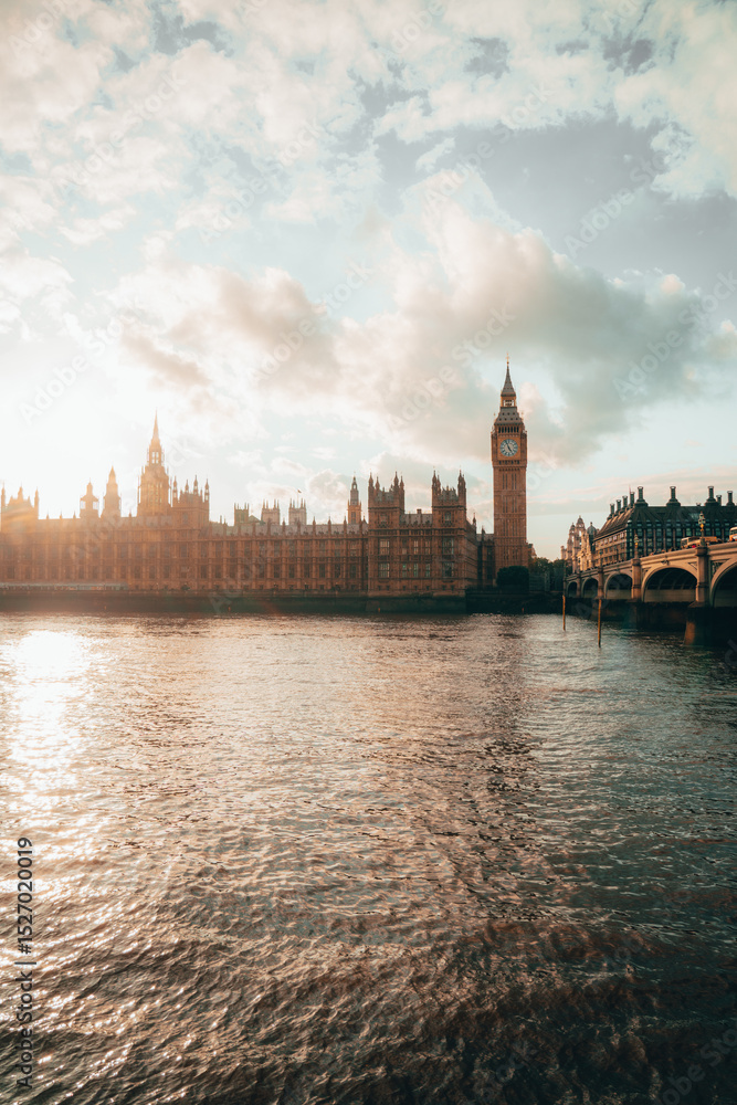 Fototapeta premium Iconic view of Big Ben with a red double-decker bus and the London Eye in the background on a cloudy day in London.