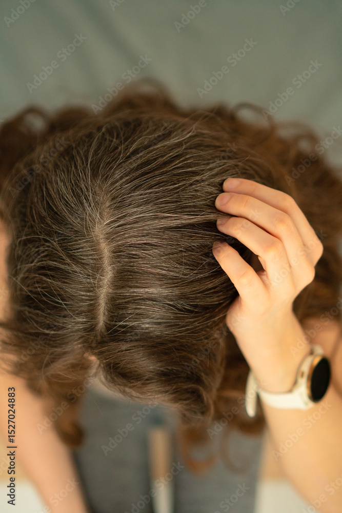 Naklejka premium Close-up top view of mature woman grasping her head, showing natural gray hair. Concept of aging, beauty, hair care, body awareness, and embracing natural changes with confidence.