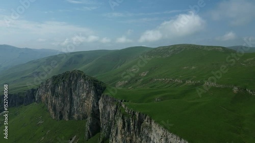 Beautiful panoramic view of green mountains with rocky formations, covered in lush grass, captured by drone against a clear blue sky.
