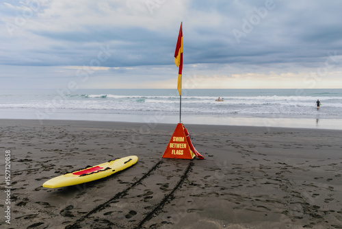 Fotografie Swimmers and surfers enjoy the ocean safely between the red and yellow surf lifesaving flags on a beach in New Zealand
