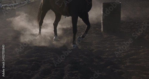 Cinematic, silhouette low shot of horse and rider kicking up dust as they run around ring - slow motion