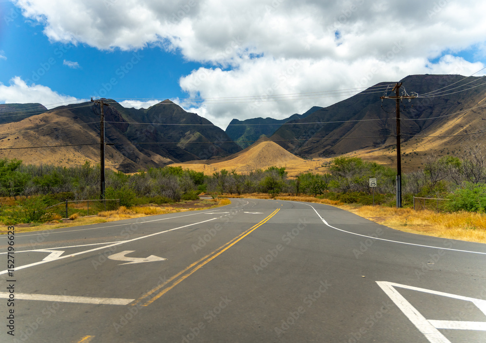Naklejka premium Road curves through a valley with mountains under a blue sky with white clouds.