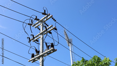 Electric wires on poles. High-voltage electric wires with fuses to prevent backflow of energy to the grid on poles on a blue sky background and field lights with copy space. selective focus