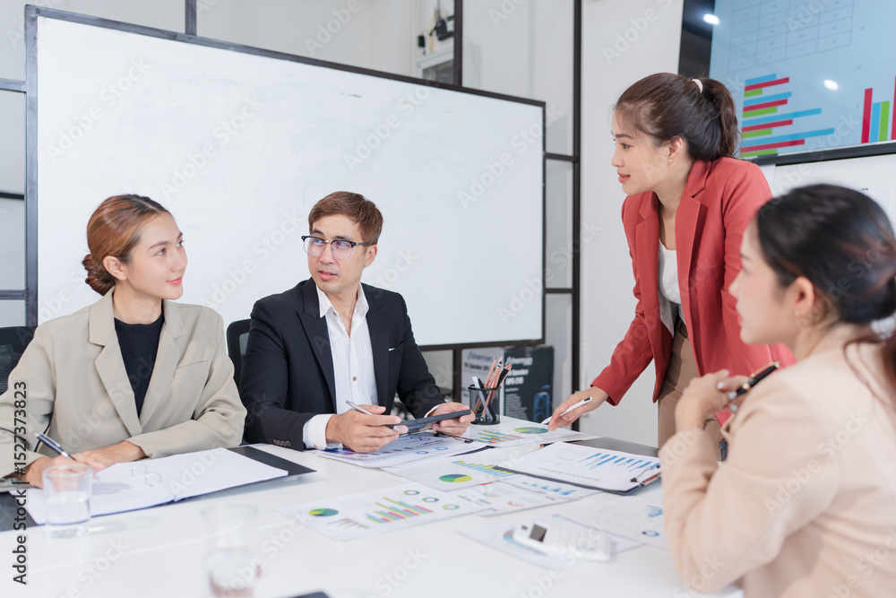 Fototapeta premium Group of Asian businesspeople sit at a table with graph paper in a meeting.