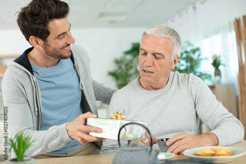 фотографія mature son congratulating elderly father giving him birthday gift