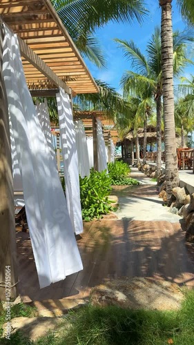 Vietnam, developing white curtains on beach by pavilion. Sun loungers with stoles, wind rippling fabrics, beautiful wedding atmosphere, paradise vacation in the Maldives, palm trees all around