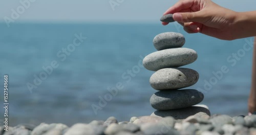 Delicately balancing pebbles by hand on serene ocean beach, creating meditative stone stack representing tranquility and mindful connection with nature's harmony