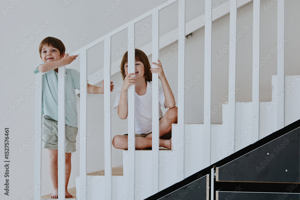 Obraz premium Two playful children enjoying their time on a staircase, showcasing joy and innocence, with bright colors and a minimalist background.