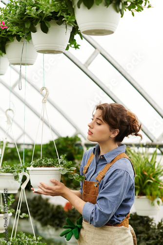 Konstfotografi Young woman tending to beautiful hanging plants in a vibrant greenhouse