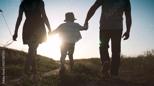 Family walking in summer day in beautiful landscape, parents lifting son up. Love and care, mother, father and little boy holding hands, woman carrying bright balloons, celebrate birthday of child