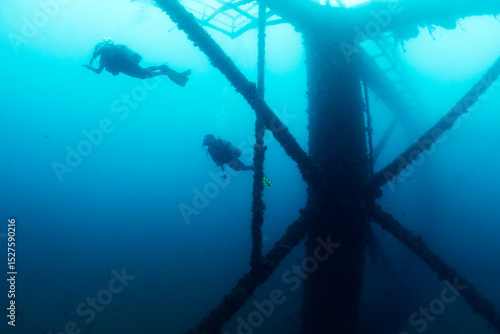 unrecognizable divers diving next to the structure of a sunken wreck in the sea, concept of scuba diving and underwater adventure, copy space for text, copy space for text