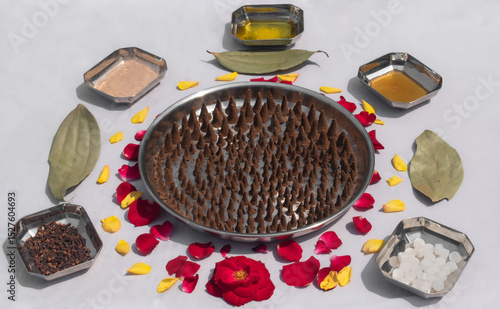Traditional home made incense cones (dhoop) arranged on a plate, surrounded by natural key ingredients like rose petals, camphor, honey, sandalwood powder, cow ghee, cloves, bay leaf.