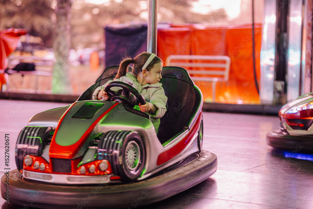 Fototapeta premium Little girl driving bumper car at amusement park