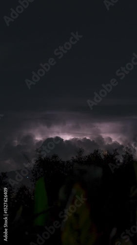 Vertical video. Multiple Lightning Strikes Illuminate Towering Thunderclouds Above Mountain Range at Night on a Tropical Island in Continuous Time-Lapse Sequence