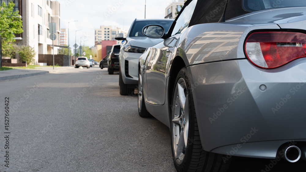 Line of parked cars along a city street in a residential area, captured from a low rear-side angle in daylight. Line of parked cars along a city street in a residential area, captured from a low rear-side angle in daylight.