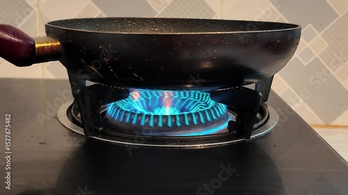 Close up of a blue flame on a gas stove burner in a dark kitchen, highlighting the energy and heat used for cooking