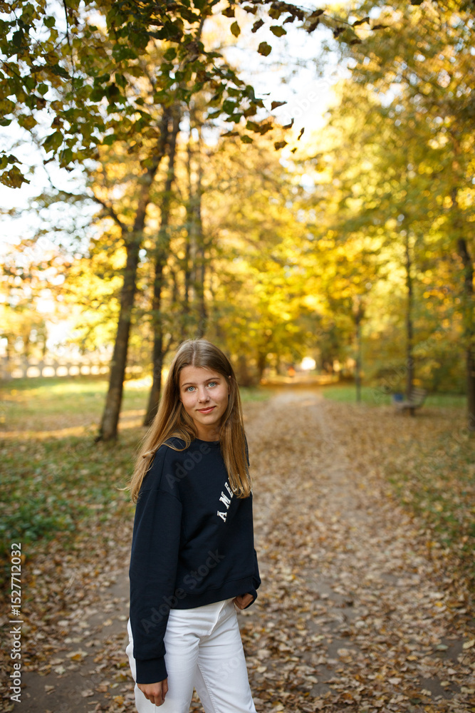 Young woman walking through an autumn park, looking back with a smile. Golden leaves cover the path, sunlight filtering through trees. Hair in motion adds energy and a joyful, carefree feel. Young woman walking through an autumn park, looking back with a smile. Golden leaves cover the path, sunlight filtering through trees. Hair in motion adds energy and a joyful, carefree feel.