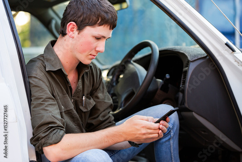 teenaged Aussie young man sitting in his car holding mobile phone device