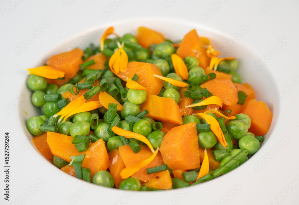 Fresh garden peas and carrots are cooked with salted butter, then garnished with chives and bright marigold flowers for an appealing and colorful side dish. Fresh garden peas and carrots are cooked with salted butter, then garnished with chives and bright marigold flowers for an appealing and colorful side dish.