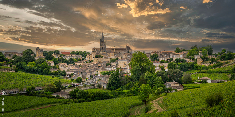 Naklejka premium Springtime brings vibrant greenery to the Bordeaux vineyards surrounding the charming village of Saint-Emilion, showcasing picturesque hills and historical architecture.