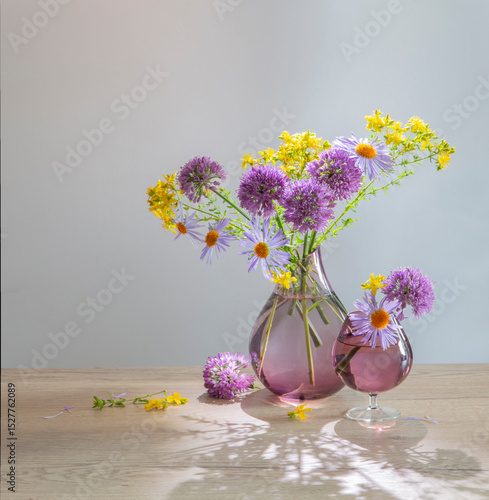 purple and yellow flowers in glass modern vase on wooden table in sunlight