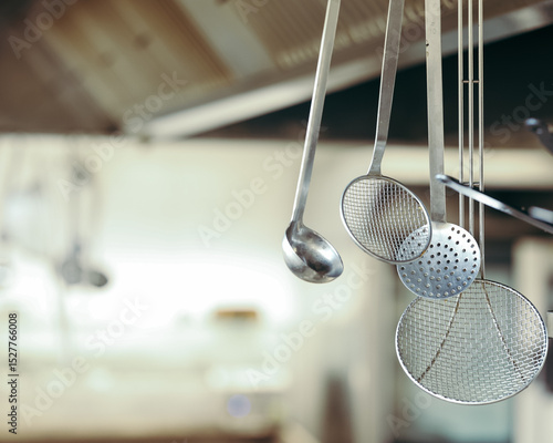 Stainless steel kitchen utensils hanging in a professional kitchen. Focus on ladles and skimmers with shallow depth of field.