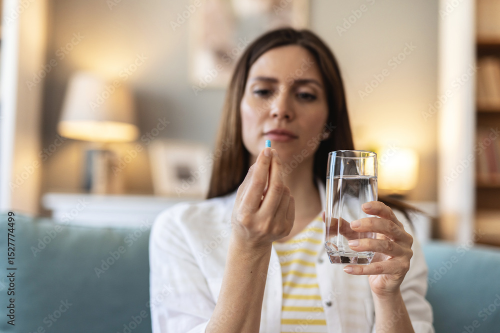 Cropped shot of an unrecognizable woman sitting alone at home and holding her medication before taking them with water. Cropped shot of an unrecognizable woman sitting alone at home and holding her medication before taking them with water.